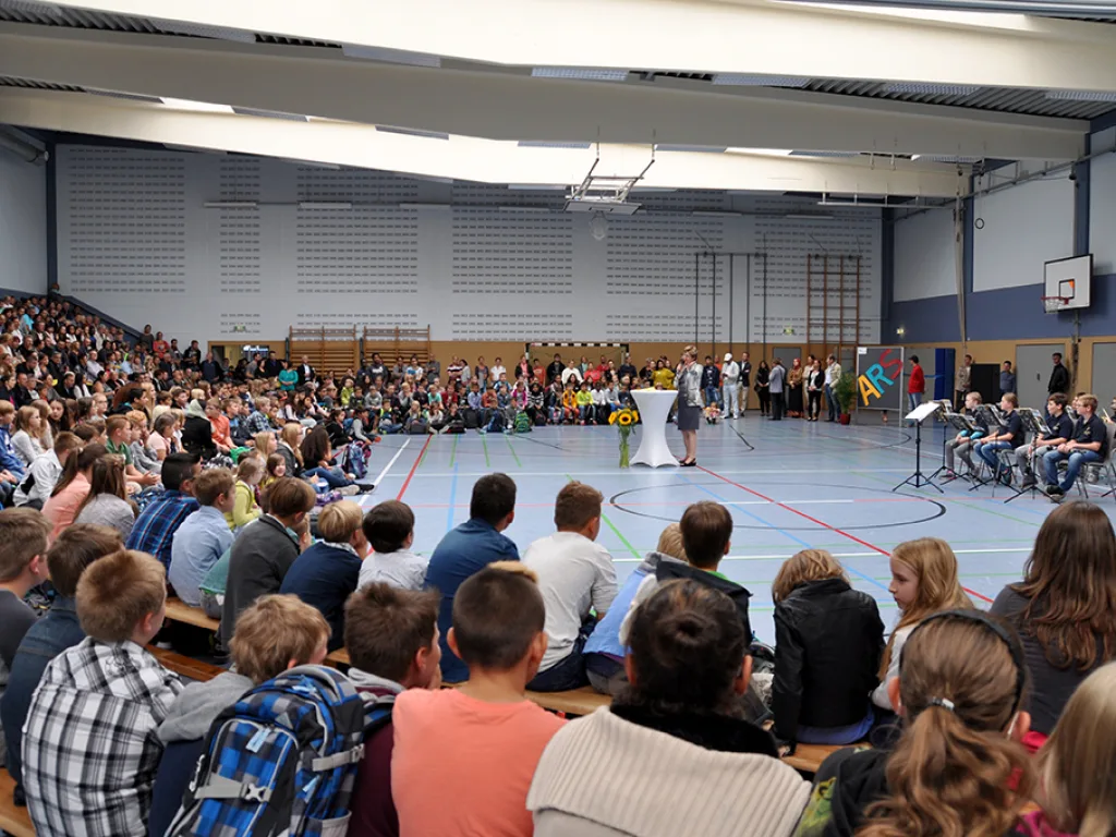 Viele Kinder und Gäste sitzen bei der Feier auf dem Hallenboden.